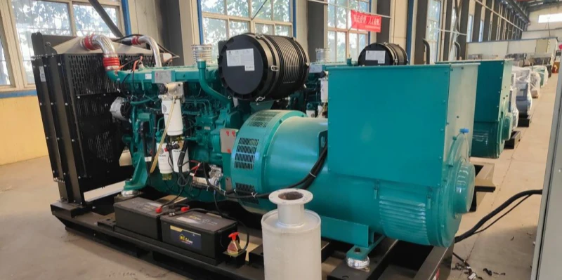 Several large teal-coloured diesel generator units lined up inside a spacious industrial workshop. Each generator has a diesel engine, large alternator, black radiator fan, exhaust piping, control panels, and batteries mounted on a metal base. The floor is concrete, with natural light coming through windows in the background.