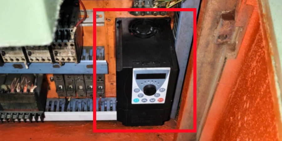 Close-up of a black variable frequency drive unit mounted inside an orange electrical control panel, featuring a digital display, control buttons, and a rotary knob, with surrounding terminal blocks and wiring