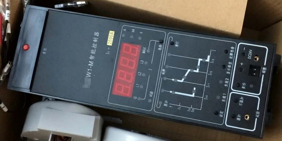 A black rectangular electronic trip unit for a 2000A air circuit breaker, shown inside a cardboard box on a workbench. The front panel has a large red LED digital display, phase indicators L1, L2, L3, current setting labels (Ir, Ii, Is, Ig), a time-current characteristic curve diagram with adjustable points, parameter adjustment buttons and knobs for long delay, short delay, instantaneous, and ground fault protection, test mode switch, red test button, DC24V power input jack, status and fault indicator lights, and English-labeled sections for settings, test, load, and trip functions.