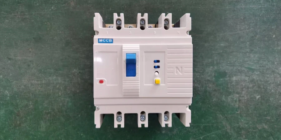A beige molded case circuit breaker (MCCB) with integrated earth leakage protection placed on a green workshop floor. It features a blue ON/OFF toggle handle in the center, top terminals labeled 1, 3, 5 for phases and N for neutral, small blue indicator LEDs, a red test/trip button on the lower left, a yellow test button below the handle, and 'MCCB' printed in blue at the top. The unit has ribbed sides for cooling, mounting holes at the bottom corners, and includes earth leakage detection functionality for ground fault protection.