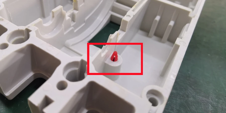 Close-up inside an opened molded case circuit breaker: red-tipped test button on a white cylindrical base, circled in red