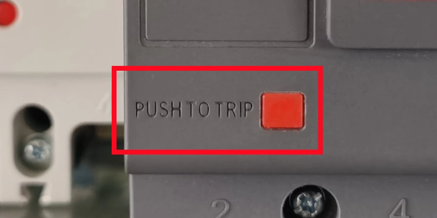 Close-up of a gray molded case circuit breaker showing the red rectangular test button with embossed text 'PUSH TO TRIP'