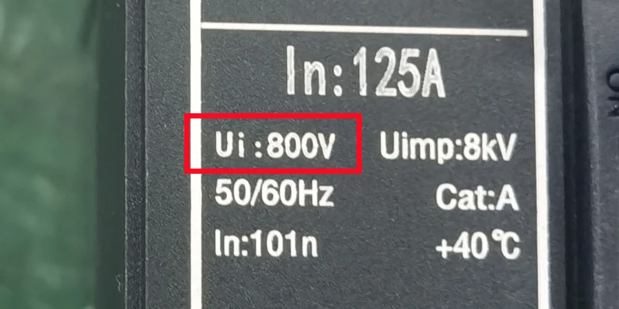 Close-up view of a black MCCB label with white text, featuring a red rectangular highlight around 'Ui : 800V', along with specifications including In:125A, Uimp:8kV, 50/60Hz, Cat:A, In:101n, and +40 °C